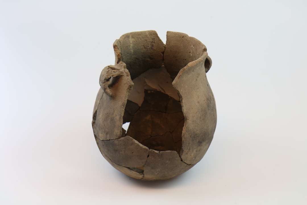 N�sten helt kar. �Rand: 13.5 cm.�Bug: 18 cm.�Bund: 9 cm.�H�jde 20 cm.�Randen er tynd og rundet. Overgang til bugen er j�vn. �2 cm under randen er  2 b�ndformede hanke (den ene er lidt deform, �den anden skaller af i den ene side).�Bunden buer en anelse indad. �Godset er fint, overfladen j�vn (skaller af flere steder).�Farve: Gr�brun. �Karret er sammensat. ��